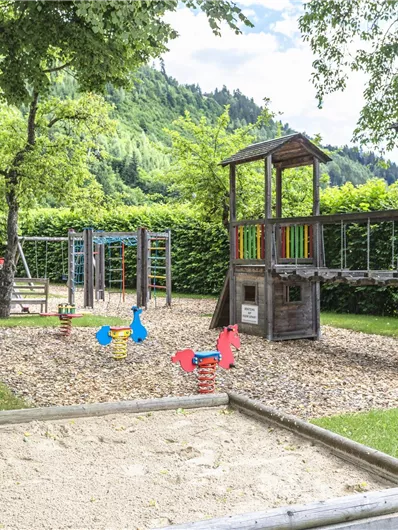 A beautiful playground with a slide, swings, and a sandbox. Surrounded by trees and green grass, ideal for children to play.