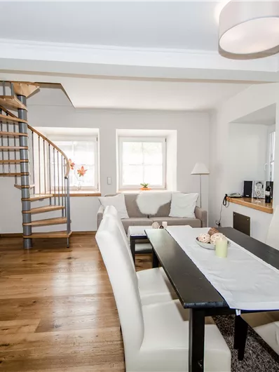 Eine moderne Küche mit einem Esstisch und hellen Stühlen. Eine Treppe führt zu einem oberen Bereich.