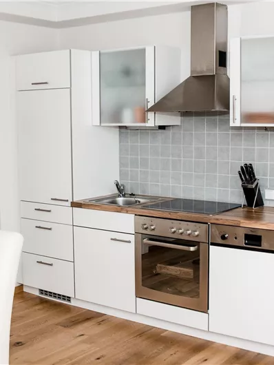 Een moderne keuken met witte kasten en een houten aanrecht. Ze is uitgerust met een fornuis, een koelkast en keukenaccessoires.