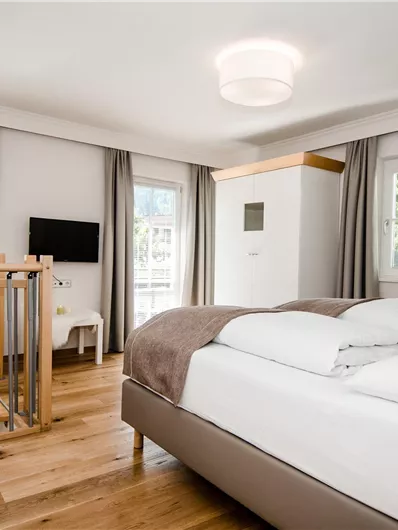 Ein modernes Schlafzimmer mit einem großen Doppelbett und Holzfußboden. Große Fenster lassen viel natürliches Licht herein und schaffen eine helle Atmosphäre.