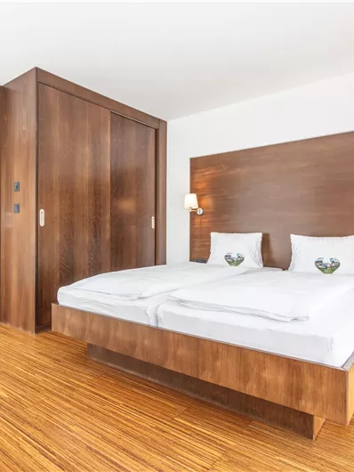A modern bedroom with two single beds and warm wooden details. The room is bright and friendly, ideal for relaxation.