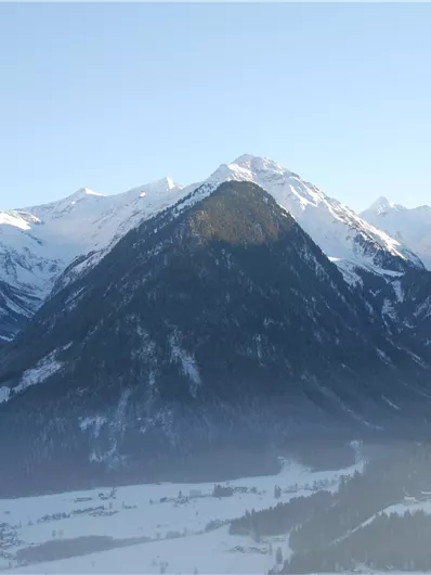 Eine beeindruckende Berglandschaft mit schneebedeckten Gipfeln. Im Vordergrund ist ein gewaltiges, ruhiges Tal zu sehen.