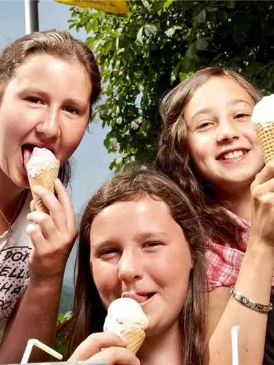 Drie meisjes genieten van ijs in wafels. Ze lachen en hebben plezier op een zonnige dag.