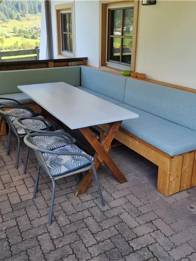 Ein gemütlicher Essbereich auf einer Terrasse mit einer großen Tischplatte und einer Eckbank. Sechs Stühle umgeben den Tisch und bieten Platz für Geselligkeit.