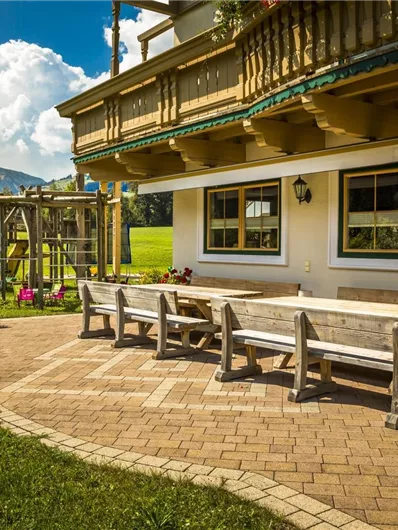 Een uitnodigende buitenruimte met een houten bank en een grote tafel. Op de achtergrond zijn zacht glooiende heuvels en een blauwe lucht met wolken te zien.