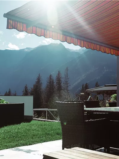 A cozy terrace with a view of the mountains and a sunny atmosphere. The green meadows and the blue sky create a relaxed mood.