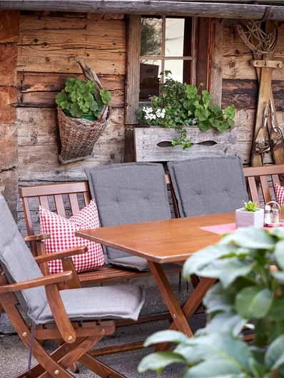 Een gezellige buitenruimte met een houten tafel en stoelen. Bloeiende planten en rustieke decoratie zorgen voor een uitnodigende sfeer.