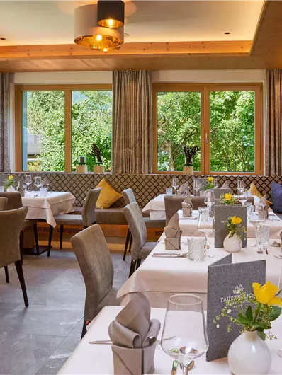 Een elegant restaurant met lichte tafels en stoelen. Grote ramen bieden uitzicht op de groene omgeving.