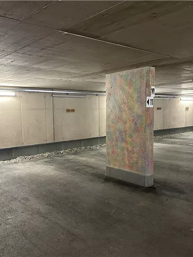 Ein Parkplatz mit grauen Wänden und bunten Säulen. Die Beleuchtung sorgt für eine helle Atmosphäre.