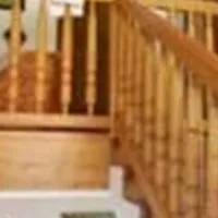 Ein heller Flur mit einer Holztreppe und einem Geländer. An den Wänden hängen einige Bilder und Fotografien.