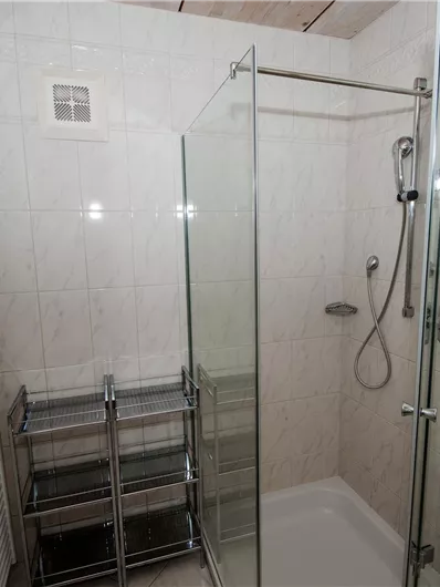 Ein modernes Badezimmer mit einer Glasduschkabine und einem Handtuchheizkörper. Der Boden ist gefliest und die Wände sind hell gefliest.