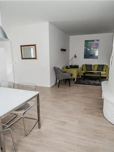 Ein modernes Wohnzimmer mit einem Esstisch und Stühlen. Im Hintergrund sind ein Sofa und ein Kamin zu sehen.