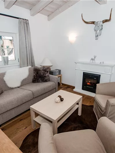 Ein gemütliches Wohnzimmer mit einem modernen Sofa und zwei Sessel. Der Raum ist hell und freundlich, mit einem Kamin und ansprechenden Dekorelementen.