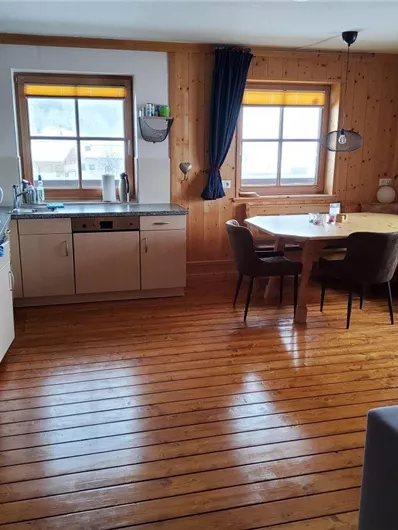 Eine gemütliche Küche mit Holzfußboden und hellen Wänden. Der Raum ist hell erleuchtet und verfügt über einen Esstisch mit Stühlen und ein Fenster mit Blick nach draußen.