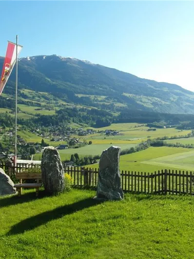 Ein schöner Ausblick auf grüne Felder und Berge. Im Vordergrund befinden sich einige Steine und eine Fahne.