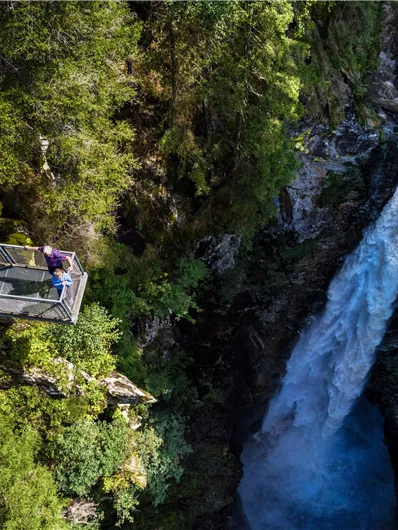 A beautiful waterfall flows through a green landscape. An observation deck offers a stunning view of nature.