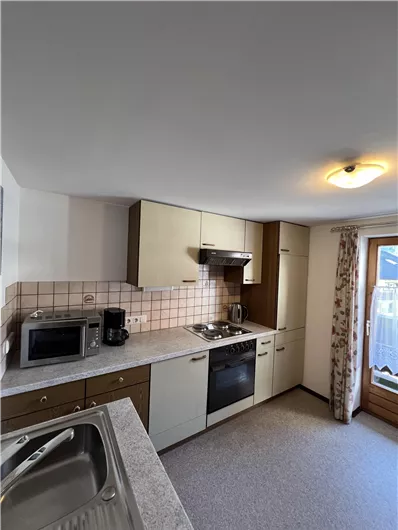 A modern kitchen with bright cabinets and a large window. It features a stove, a microwave, and a sink.