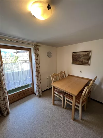 A cozy dining area with a large wooden table and chairs. Light comes in through the window, creating an inviting atmosphere.
