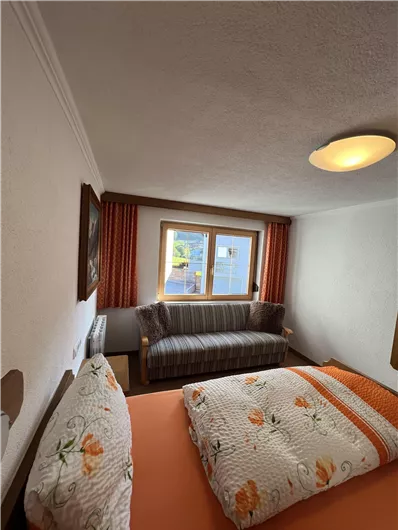 A cozy bedroom with a large bed and a sofa. The room has windows with a view and bright, inviting colors.