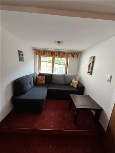 A cozy living area with a gray couch and a small table. The room has windows that let in natural light.