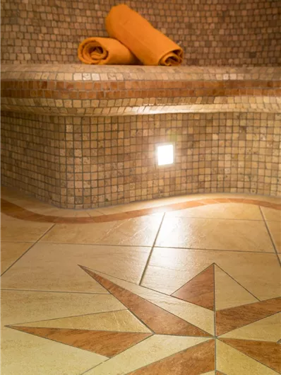 Een ontspannend wellnessgebied met een tegelbank en een decoratief vloermozaïek. Daarop ligt een oranje handdoek.