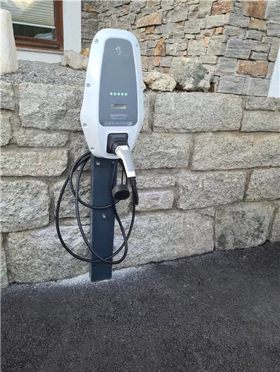 A charging station for electric cars at a stone wall. It is ready for use and displays charging indicators.