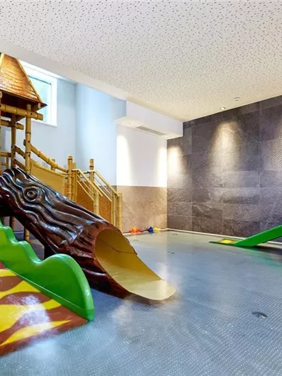 Ein Indoor-Spielbereich mit bunten Rutschen und einem Spielturm aus Holz. Der Boden ist flach und bietet Platz für Kinder zum Spielen.