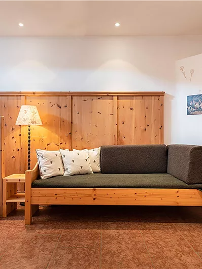Ein gemütlicher Wohnbereich mit einem Holzsofa und einer Stehlampe. Die Wände sind mit Holz verkleidet, und eine Treppe führt nach oben.
