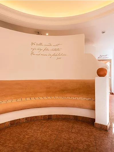 Ein helles und modernes Innendesign mit einer runden Holzbänkbänken und einer Pflanzenarrangements. Die Wände sind schlicht und mit dekorativen Schriftzügen gestaltet.