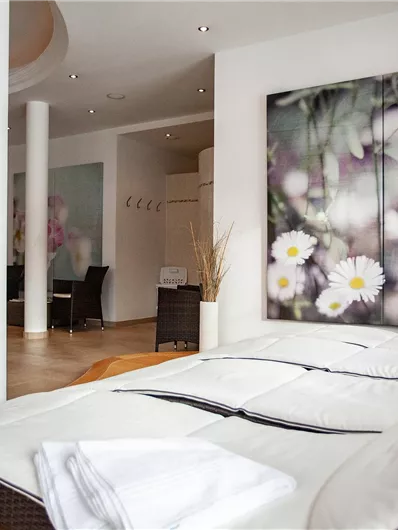An elegant room with two beds and modern decor. A large painting of flowers hangs on the wall.