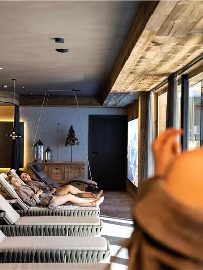 Ein moderner Wellnessbereich mit bequemen Liegen und großen Fenstern. Im Hintergrund entspannen Gäste und genießen die Ruhe.