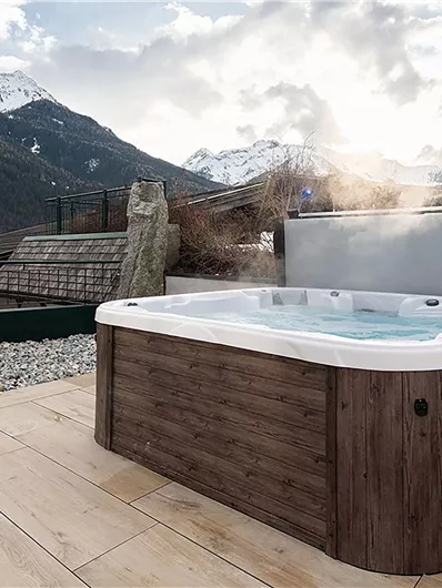 Ein moderner Whirlpool auf einer Terrasse mit Blick auf die Berge. Die Umgebung ist ruhig und einladend, perfekt zum Entspannen.