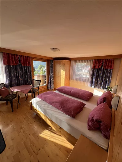 A cozy bedroom with two beds and purple pillows. Large windows provide plenty of daylight and offer a view of the surroundings.