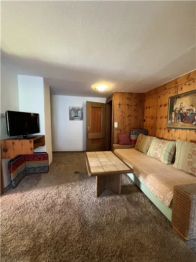 A cozy living room with a sofa and a table. Pictures hang on the wall, and there is a television in the corner.