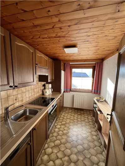 A small kitchen with wood paneling and a window view. The equipment includes a stove, a sink, and a table.