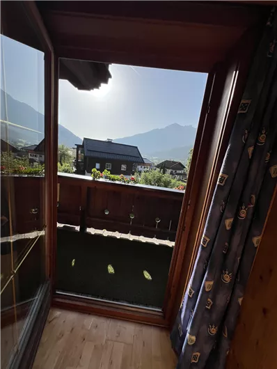 A view from a balcony over a picturesque mountain landscape. The sun shines behind the mountains and it is a clear, beautiful day.