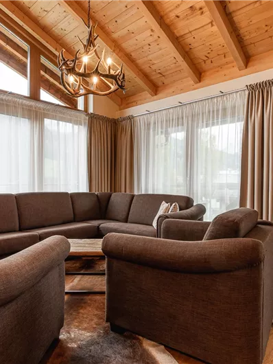 A cozy living room with a large, cushioned sofa and a fireplace. Large windows provide plenty of natural light.