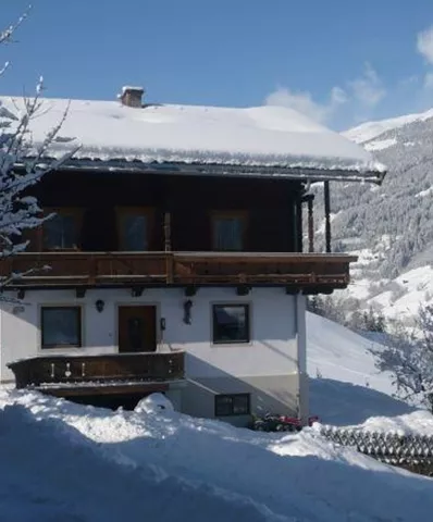 Ein schönes, schneebedecktes Berghaus mit traditioneller Architektur. Im Hintergrund sind schneebedeckte Berge und ein blauer Himmel zu sehen.