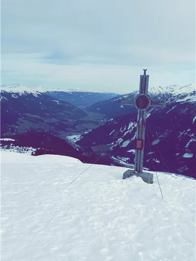 Een met sneeuw bedekte berglandschap met een hoogte marker op de voorgrond. Op de achtergrond zijn majestueuze bergen en een vallei te zien.