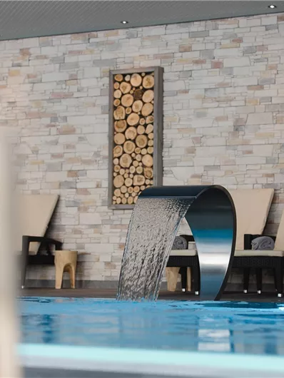 A modern wellness area with a large pool and a waterfall. The walls are decorated with wood and stone, while comfortable chairs invite you to relax.