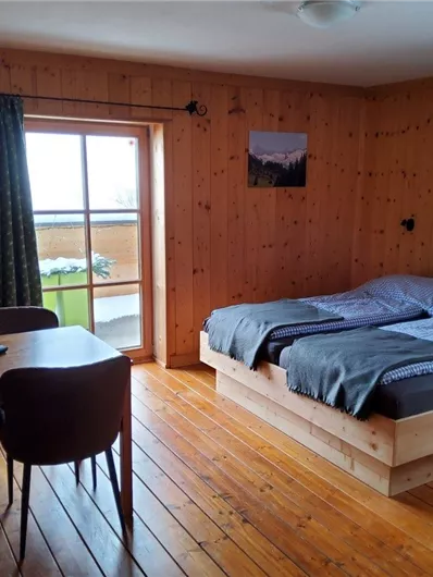 Ein gemütliches Zimmer mit Holzwänden und einem Doppelbett. Es gibt einen Tisch, Stühle und große Fenster mit Blick auf die Aussicht.