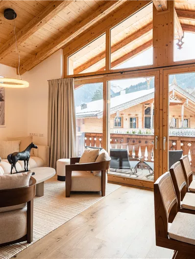 Ein helles Wohnzimmer mit großen Fenstern und einer schönen Aussicht auf die Berge. Der Raum ist modern eingerichtet mit gemütlichen Möbeln und einem Essbereich.