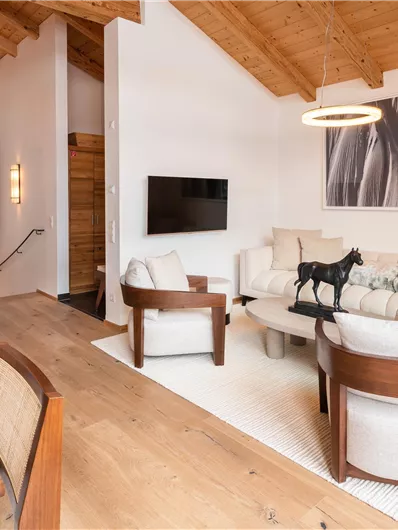 Ein modernes Wohnzimmer mit Holzdecke und stilvollen Möbeln. Es gibt einen großen Fernseher und eine elegante Dekoration.