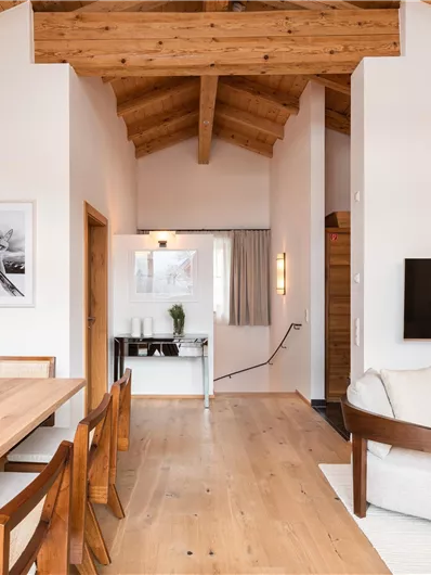 Ein modernes Wohnzimmer mit Holzdecke und großem Esstisch. Die Einrichtung ist schlicht und hell, mit einem bequemen Sofa und einer TV-Wand.