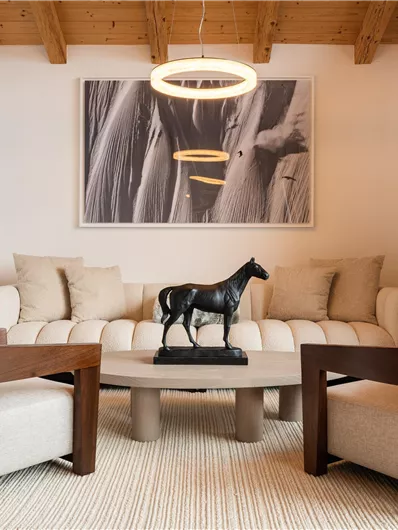 Ein modernes Wohnzimmer mit einem bequemen Sofa und zwei Sesseln. Ein Kunstwerk eines Pferdes ziert den Couchtisch und große Fenster sorgen für viel Licht.