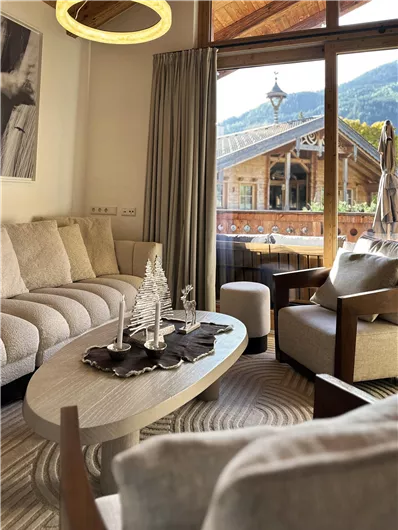 Ein gemütliches Wohnzimmer mit einem einladenden Sofa und einem runden Tisch. Große Fenster bieten einen Blick auf die Berge und einen charmanten Außenbereich.