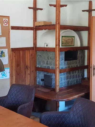 Ein gemütlicher Raum mit einem Holztisch, Stühlen und einer offenen Tür. An der Wand befindet sich ein Regal und im Hintergrund ein Kamin.