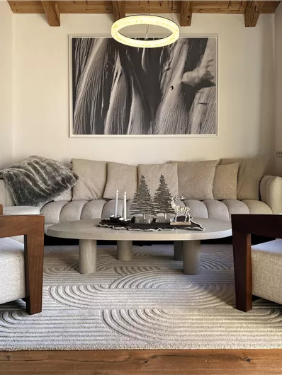 Ein modernes Wohnzimmer mit einem runden Sofa und zwei bequemen Stühlen. Die Einrichtung ist schlicht und elegant, ergänzt durch ein großes Kunstwerk an der Wand.