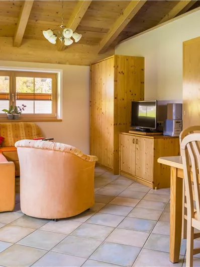 Een gezellige woonkamer met een oranje bank en een tafel. De muren zijn licht en de houten decoratie geeft een warme sfeer.