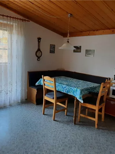 Een gezellige keuken met een eetgedeelte en een groot raam. De muren zijn licht en het houten dak zorgt voor een warme sfeer.